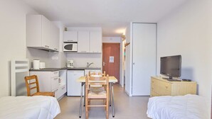 A compact room with a kitchenette, two single beds, a wooden chair, a television, and a small table. - Quiet studio with Wifi and parking in Barbotan-les-Thermes (Barbotan-les-Thermes)