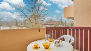 A round table with a white tablecloth, two glass cups, a metal pitcher, and a white chair on a balcony with a view of houses and trees. - South-Facing Studio with Balcony, WIFI and Pets Allowed - For 2 People (Barbotan-les-Thermes)