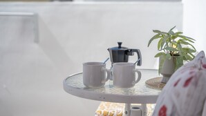 A round table with two white mugs, a coffee maker, and a potted plant on a balcony.