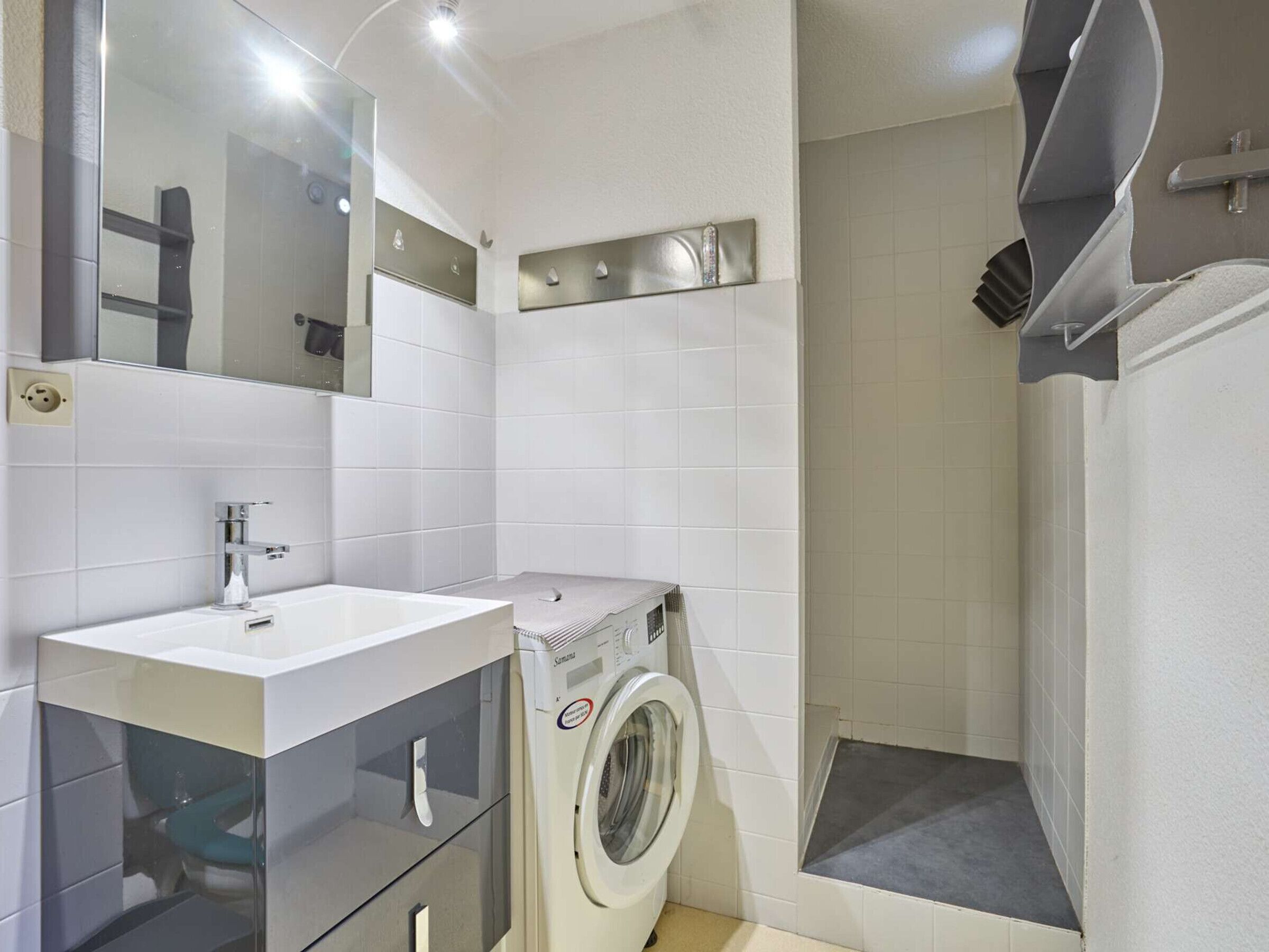 A modern bathroom with a sink, mirror, and a built-in washing machine.