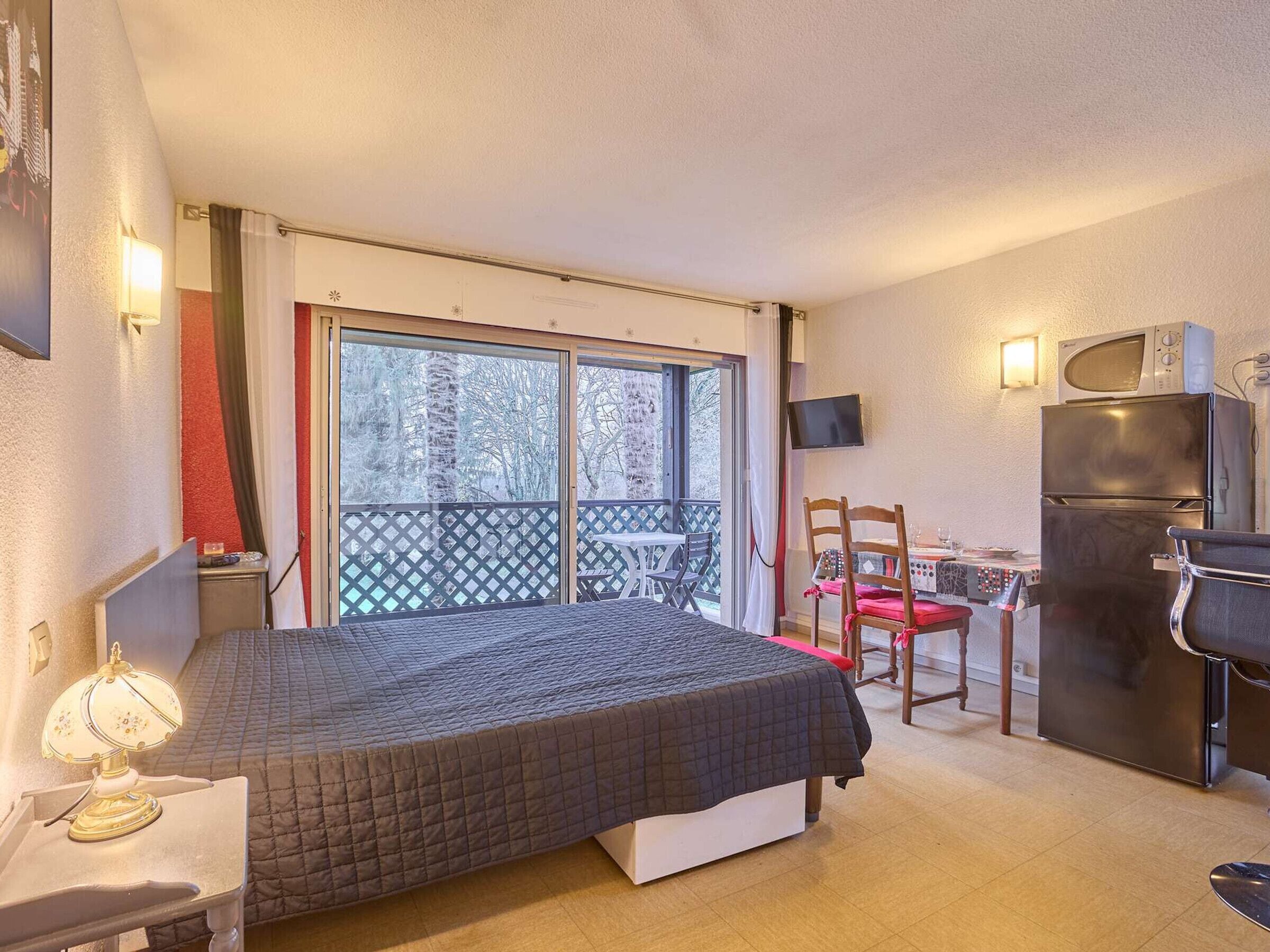 A bedroom with a bed, a desk, a chair, a TV, and a refrigerator.