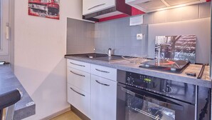 Cocina compacta con armarios blancos, horno de acero inoxidable y una pared de acento roja.