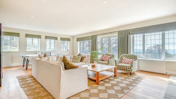 Uma sala de estar ampla com sofá, poltronas, mesa de centro e grandes janelas com vista.