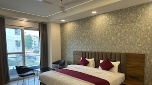 Una habitación de hotel moderna con una cama grande, una mesita de noche, una silla y vistas a la ciudad desde la ventana.