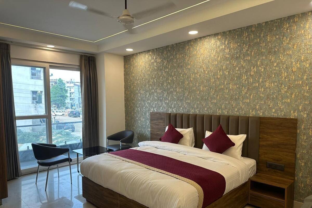 Una habitación de hotel moderna con una cama grande, una mesita de noche, una silla y vistas a la ciudad desde la ventana.