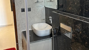Un baño moderno con ducha envuelta en vidrio, un lavamanos blanco y una pared de mármol negro.