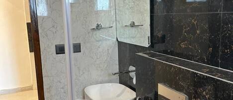 A modern bathroom with a glass-enclosed shower, a white sink, and a black marble wall.