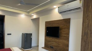 Habitación de hotel con cama, televisión montada en un panel de madera, refrigerador y unidad de aire acondicionado.