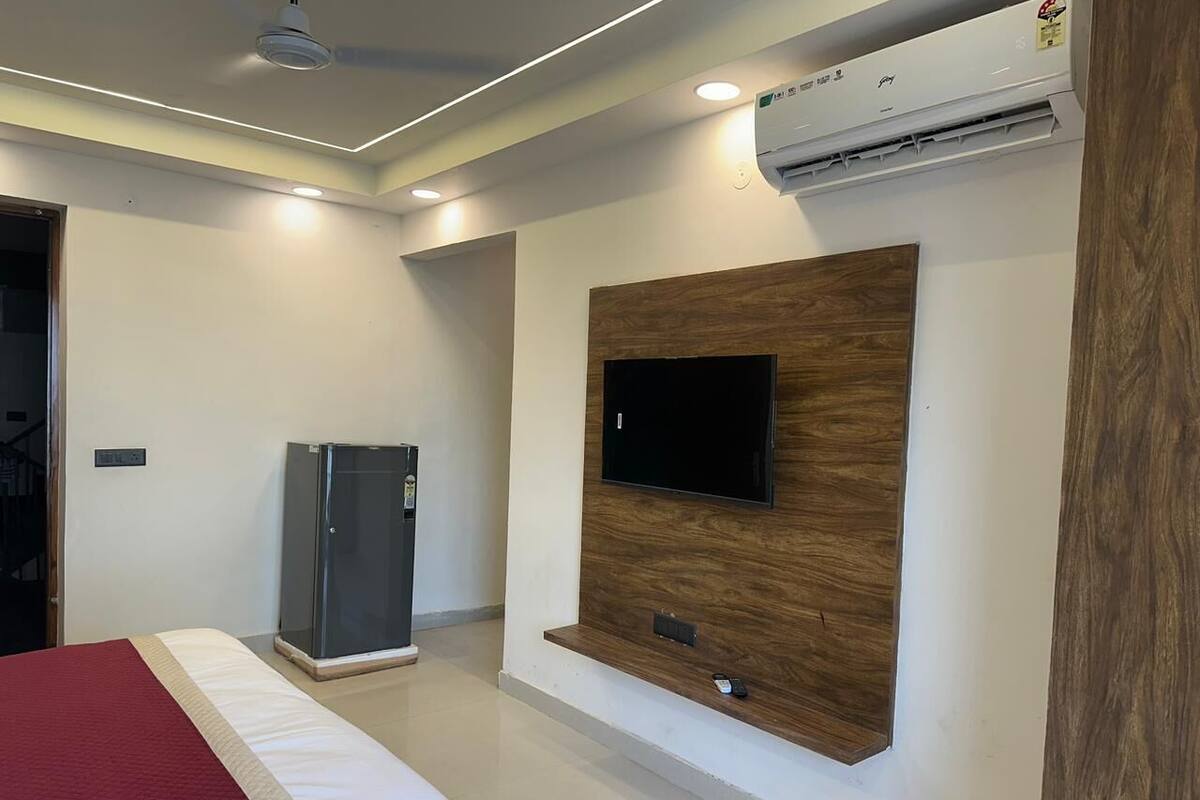 Habitación de hotel con cama, televisión montada en un panel de madera, refrigerador y unidad de aire acondicionado.