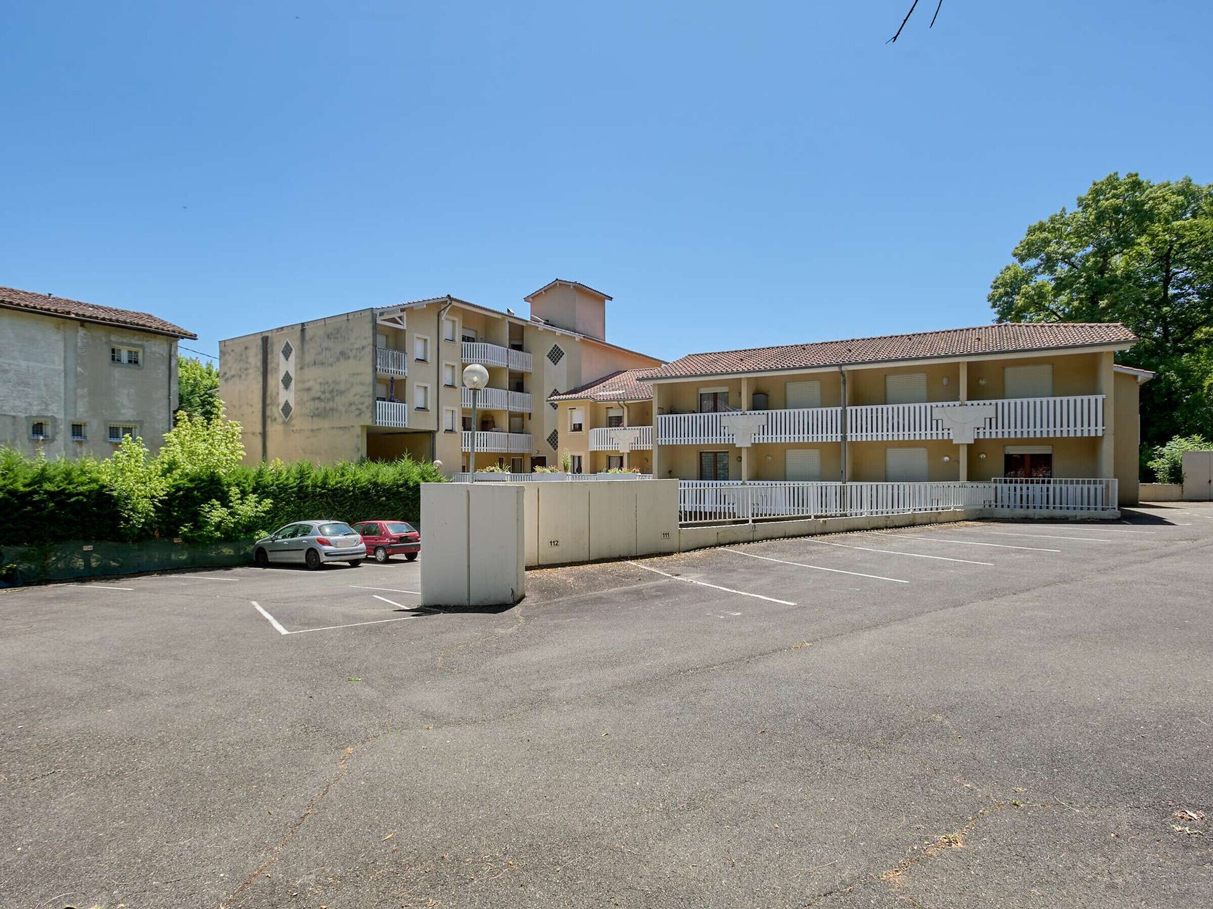 A multi-story building with balconies and a parking lot.