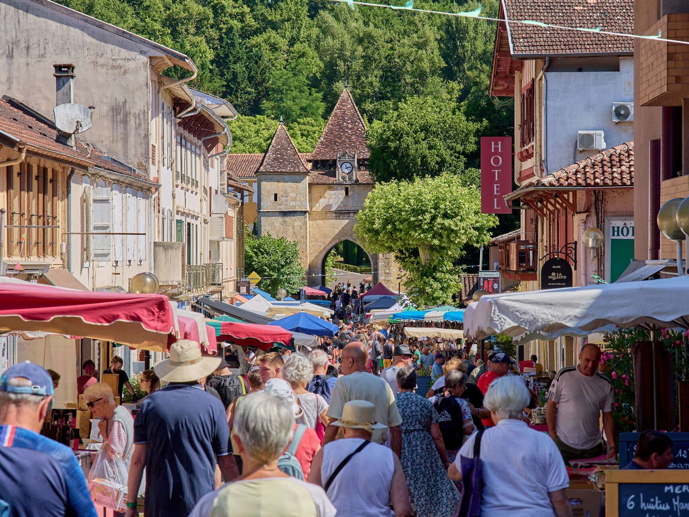 A bustling outdoor market with various stalls and a historic building with a clock tower in the background.