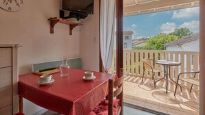 Un balcon avec une table et des chaises, un téléviseur fixé sur une étagère en bois, et une vue sur des immeubles et des arbres.