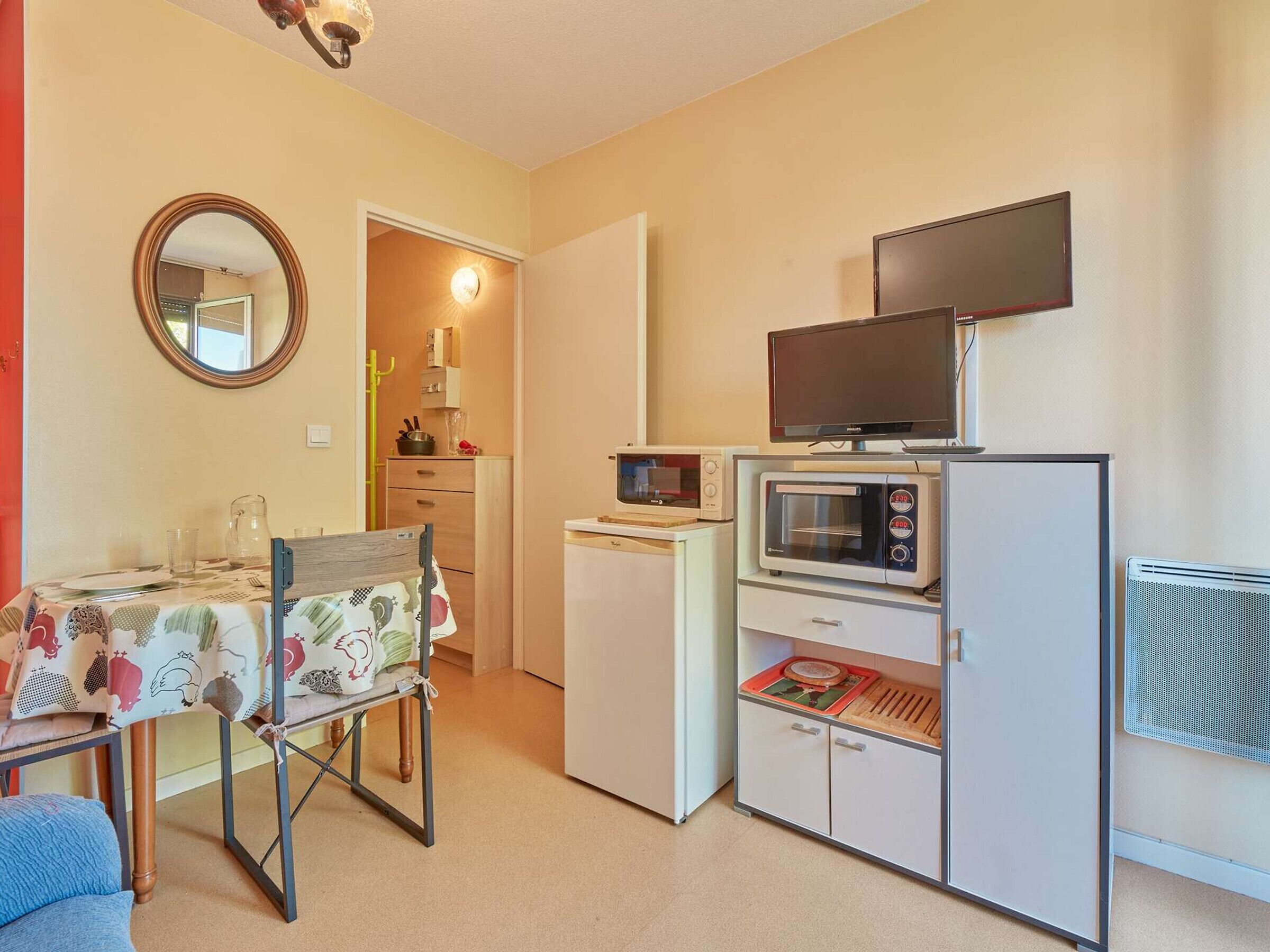 A compact kitchenette with a microwave, toaster, and a flat-screen TV on a stand.