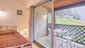 Une chambre à coucher comprenant un lit, une table de chevet, une lampe et une porte-fenêtre coulissante donnant sur un balcon équipé d’une table et de chaises.