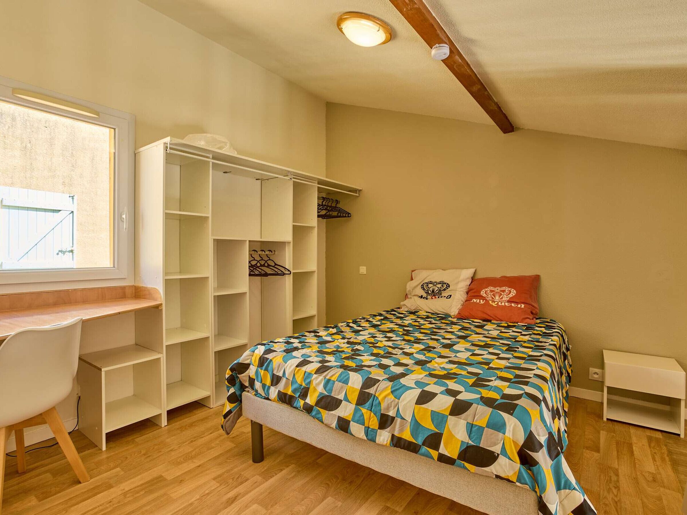 A bedroom with a bed, a desk, and a wardrobe.