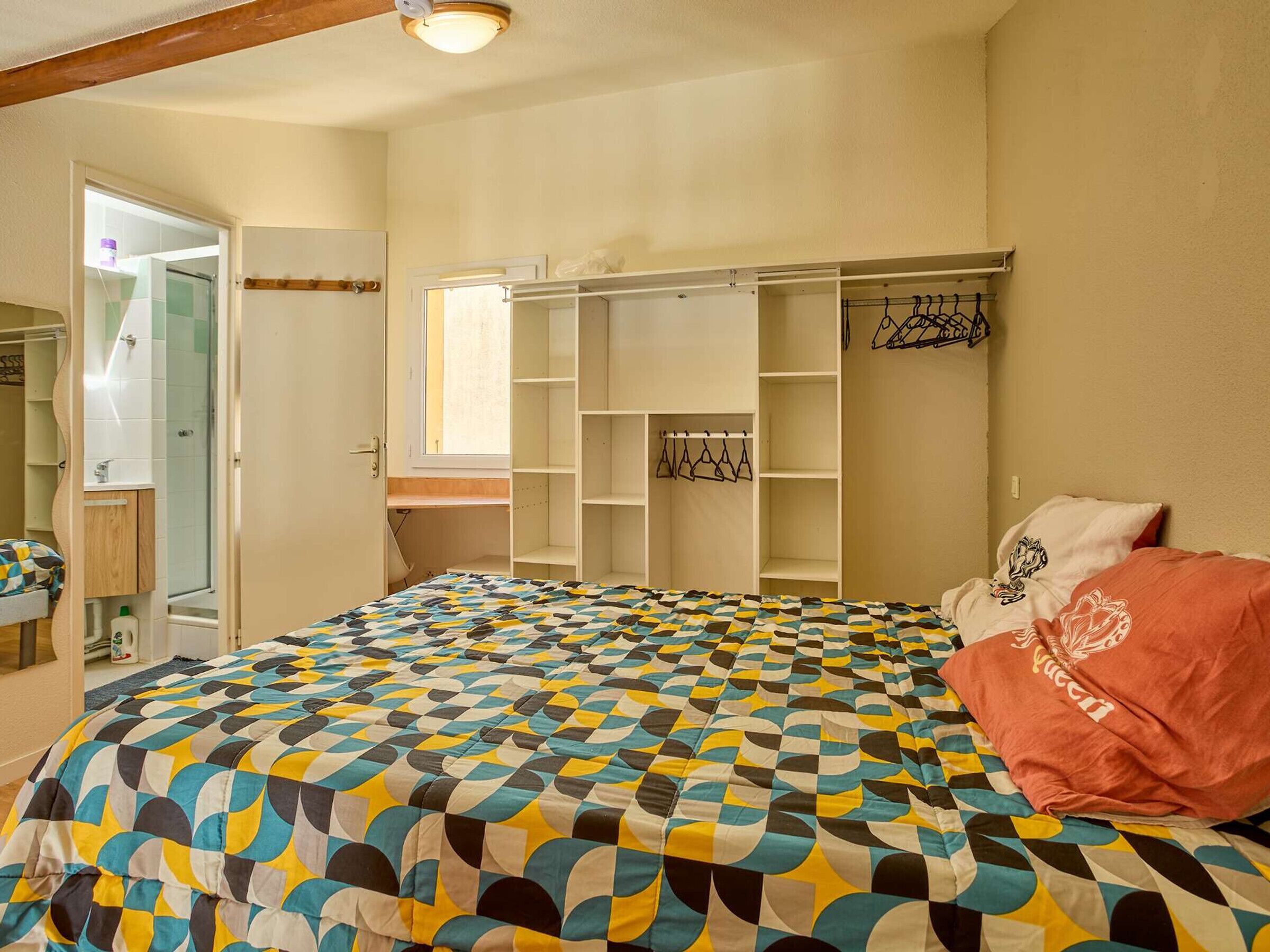 Une chambre à coucher avec un lit, une armoire, un miroir et une fenêtre.