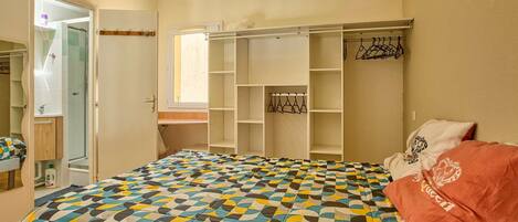 A bedroom with a bed, a wardrobe, a mirror, and a window.