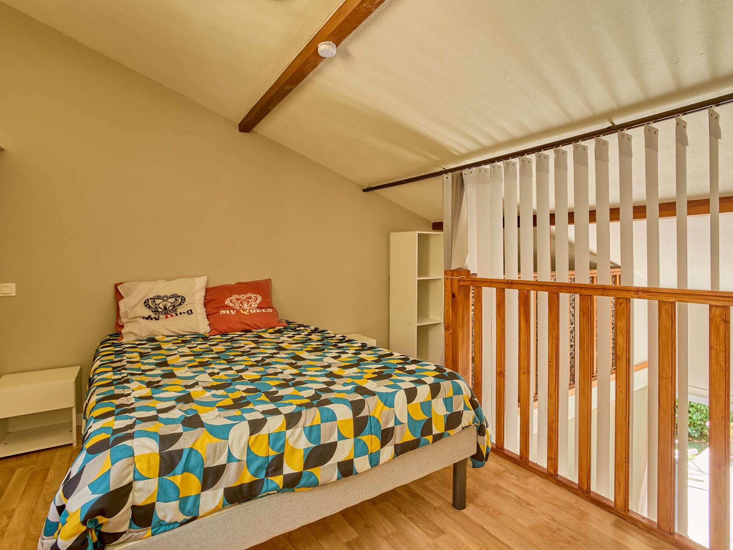 A bedroom with a bed, a white wardrobe, a wooden railing, and a ceiling light.