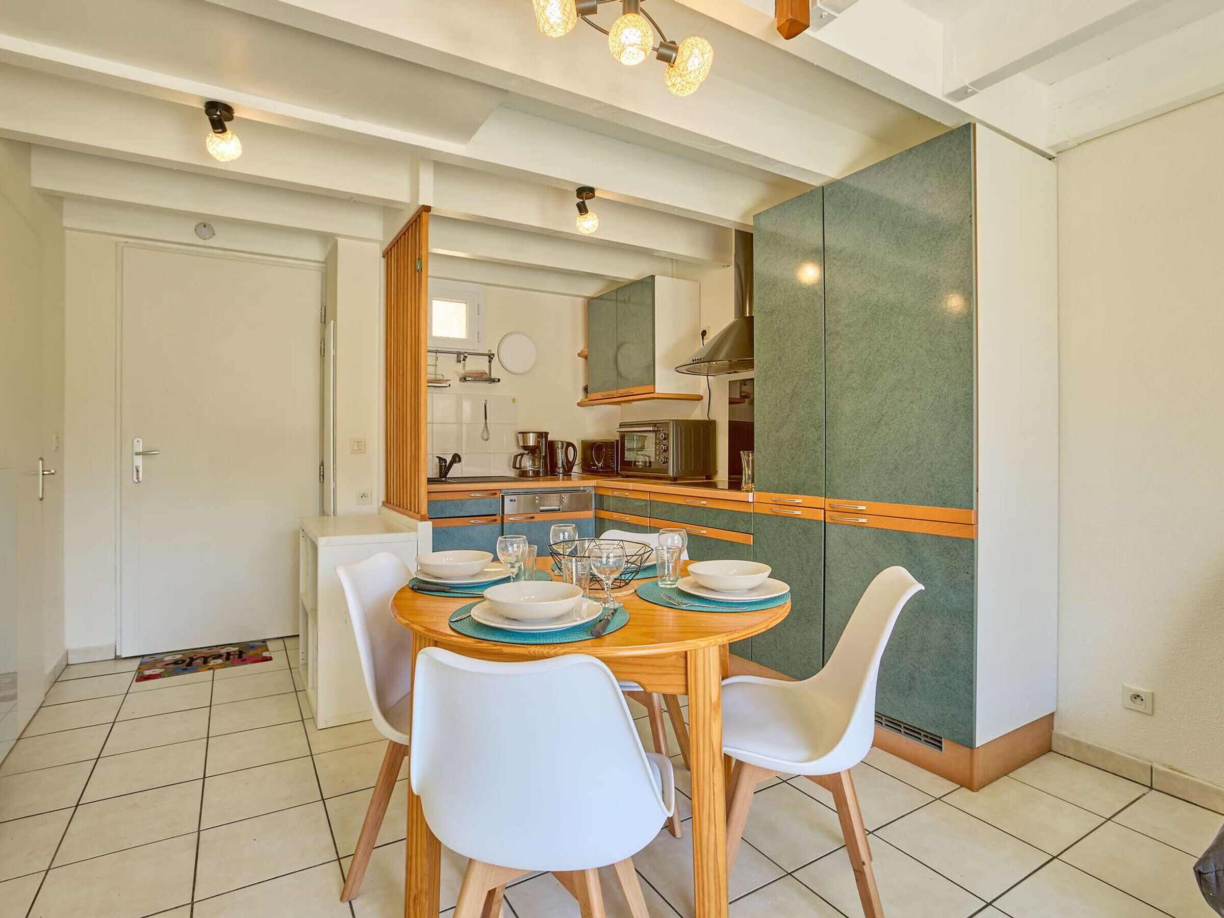 A modern kitchen with a dining area, featuring a wooden table, white chairs, and a green backsplash.