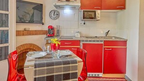 A compact kitchen with red cabinets, a microwave, a clock, and a dining area with a table set for two.