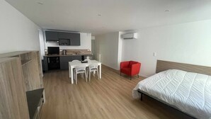 A compact hotel room with a bed, a small dining table with chairs, a red armchair, and a kitchenette in the background. - Centrally located air-conditioned studio with wifi and fully equipped kitchen (Châteauroux)