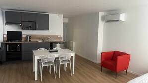 A compact kitchen with modern appliances, a dining area with white chairs, and a red armchair. - Centrally located air-conditioned studio with wifi and fully equipped kitchen (Châteauroux)