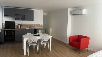 Une cuisine compacte dotée d’appareils électroménagers modernes, un coin repas avec des chaises blanches et un fauteuil rouge.