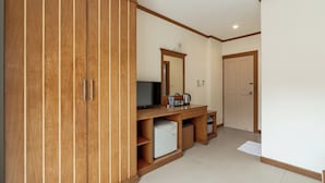 A hotel room with wooden wardrobe, a small desk with a mirror, a refrigerator, and a door leading to another room. - The Eden Park (Patong)