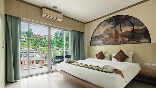 A hotel room with a large bed, a painting on the wall, and a view of greenery outside. - The Eden Park (Patong)