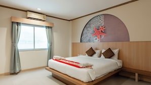 A modern hotel room with a large bed, a wall-mounted air conditioner, a large window with curtains, and a unique wall art piece. - The Eden Park (Patong)