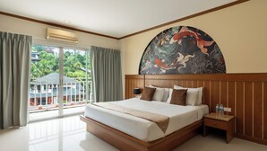 A hotel room with a large bed, a nightstand, a wall-mounted air conditioner, and a view of a building and trees through a sliding glass door. - The Eden Park (Patong)
