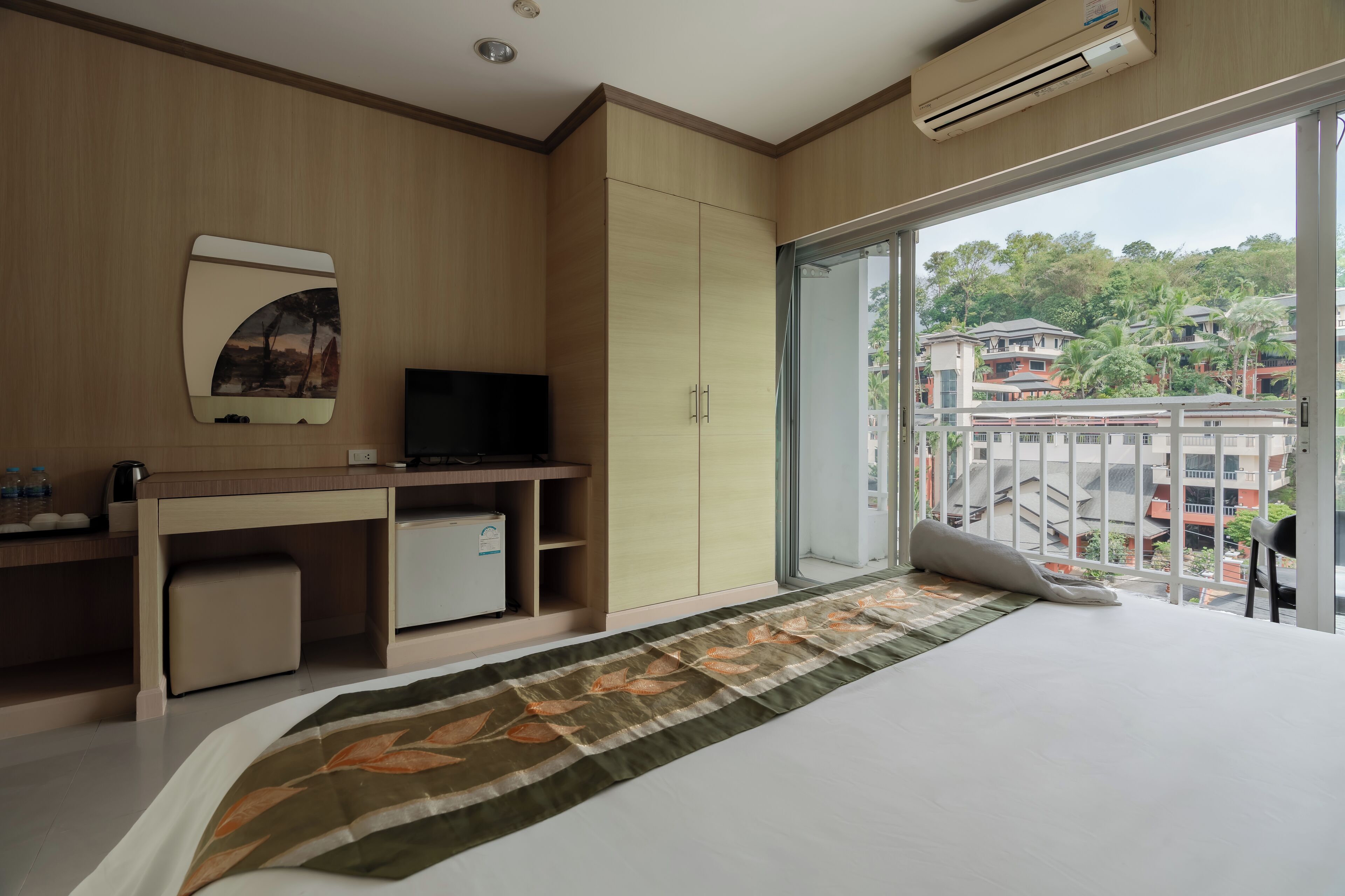 Habitación de hotel moderna con una cama, un escritorio, un televisor y un amplio ventanal con vistas a edificios y árboles.