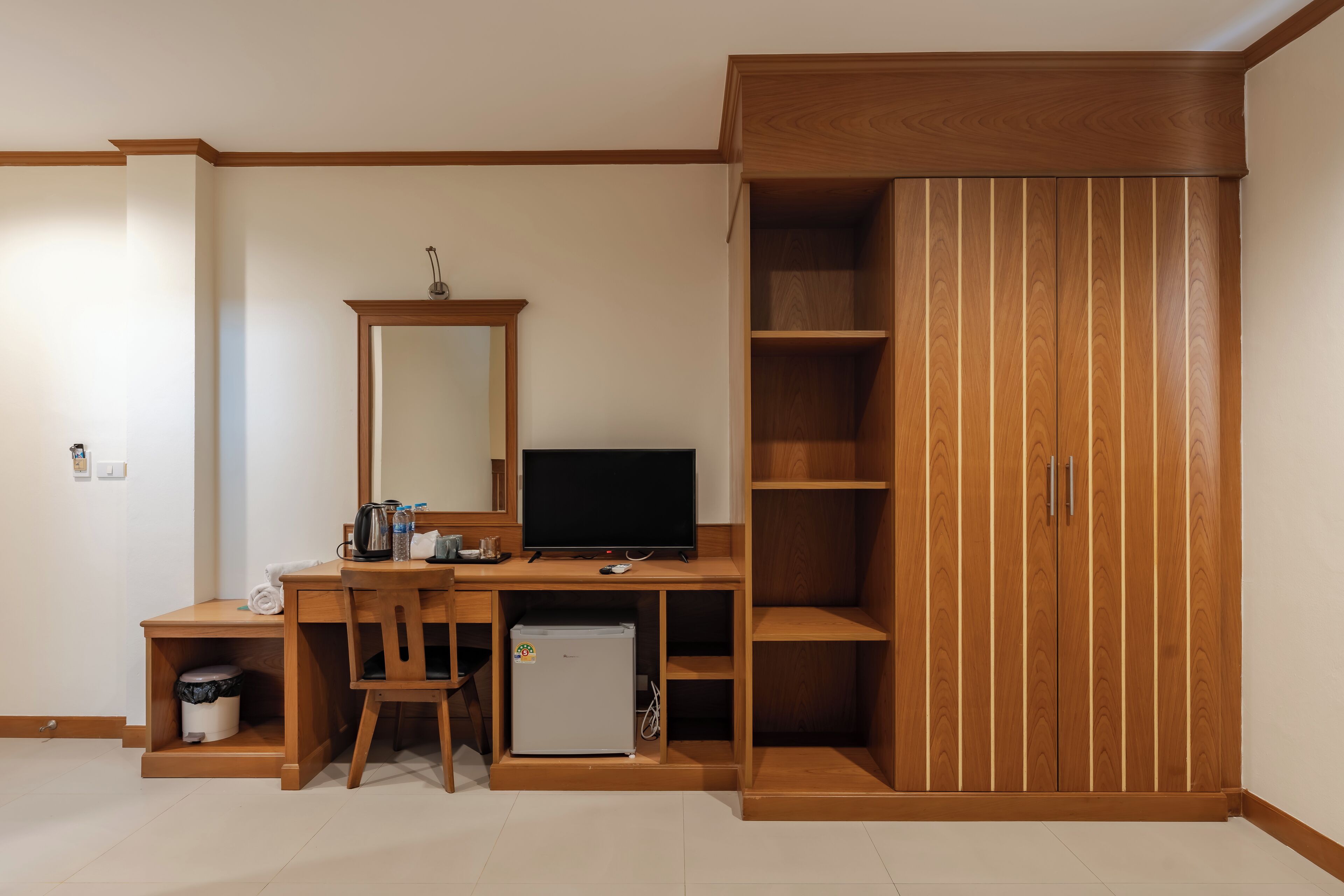 A compact room with a wooden desk, a television, a small refrigerator, and a wardrobe with multiple shelves.