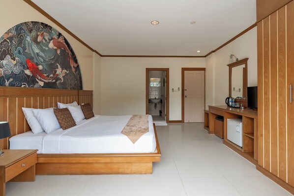 A hotel room with a large bed, wooden headboard, a painting on the wall, a small kitchenette, and a mirror. - The Eden Park (Patong)