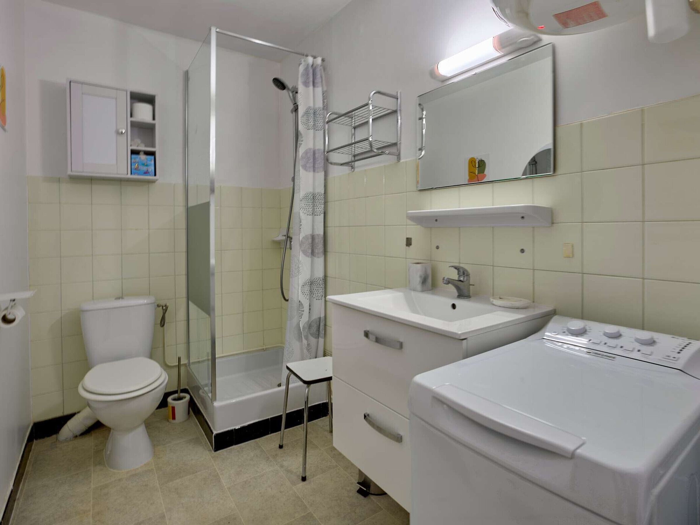 A bathroom with a toilet, shower, sink, and a washing machine.