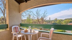 A terrace with two white plastic chairs and a small round table, a green railing, and a view of trees and buildings. - Quiet T2 near spa with Wifi and parking, pets allowed (Barbotan-les-Thermes)