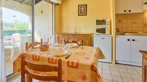 A dining area with a table set for two, a kitchen with white cabinets and a microwave, and a sliding glass door leading to an outdoor area. - Quiet T2 near spa with Wifi and parking, pets allowed (Barbotan-les-Thermes)