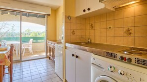 A compact kitchen with a built-in washing machine, a sink, and a small dining area with a table and chairs. - Quiet T2 near spa with Wifi and parking, pets allowed (Barbotan-les-Thermes)