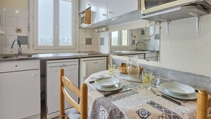 A compact kitchen with white cabinets, a microwave, and a dining area set for two with a table set with plates, glasses, and a pitcher. - Bright T2 with Balcony, WIFI, Parking, Pets Allowed (Barbotan-les-Thermes)
