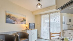 A living room with a sofa, a television, and a painting on the wall. - Bright T2 with Balcony, WIFI, Parking, Pets Allowed (Barbotan-les-Thermes)