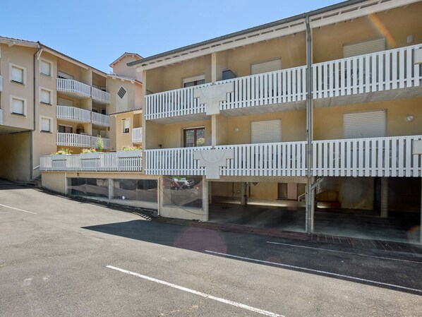A multi-story residential building with balconies and a parking area in front.