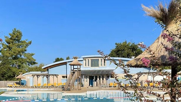 A pool area with a water slide, lounge chairs, and a building with a unique curved roof. - Bright T2 with Balcony, WIFI, Parking, Pets Allowed (Barbotan-les-Thermes)