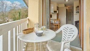 A balcony with a white table and chairs, a wicker basket, and a microwave visible through an open door. - Bright T2 with Balcony, WIFI, Parking, Pets Allowed (Barbotan-les-Thermes)