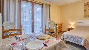 Habitación de hotel con una mesa de comedor preparada para dos personas, una cama con cubrecama acolchado, una mesita de noche de madera y un cartel en la pared.