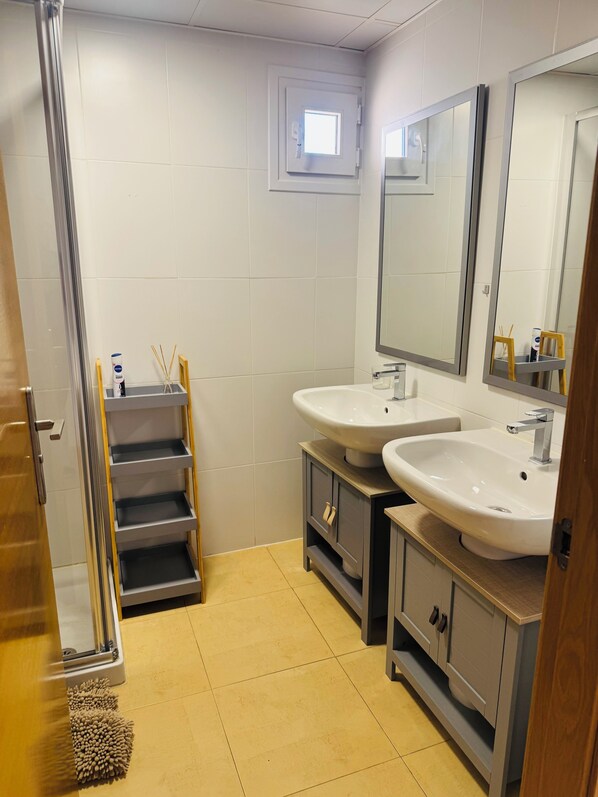 A bathroom with two sinks, a shower, and a window.