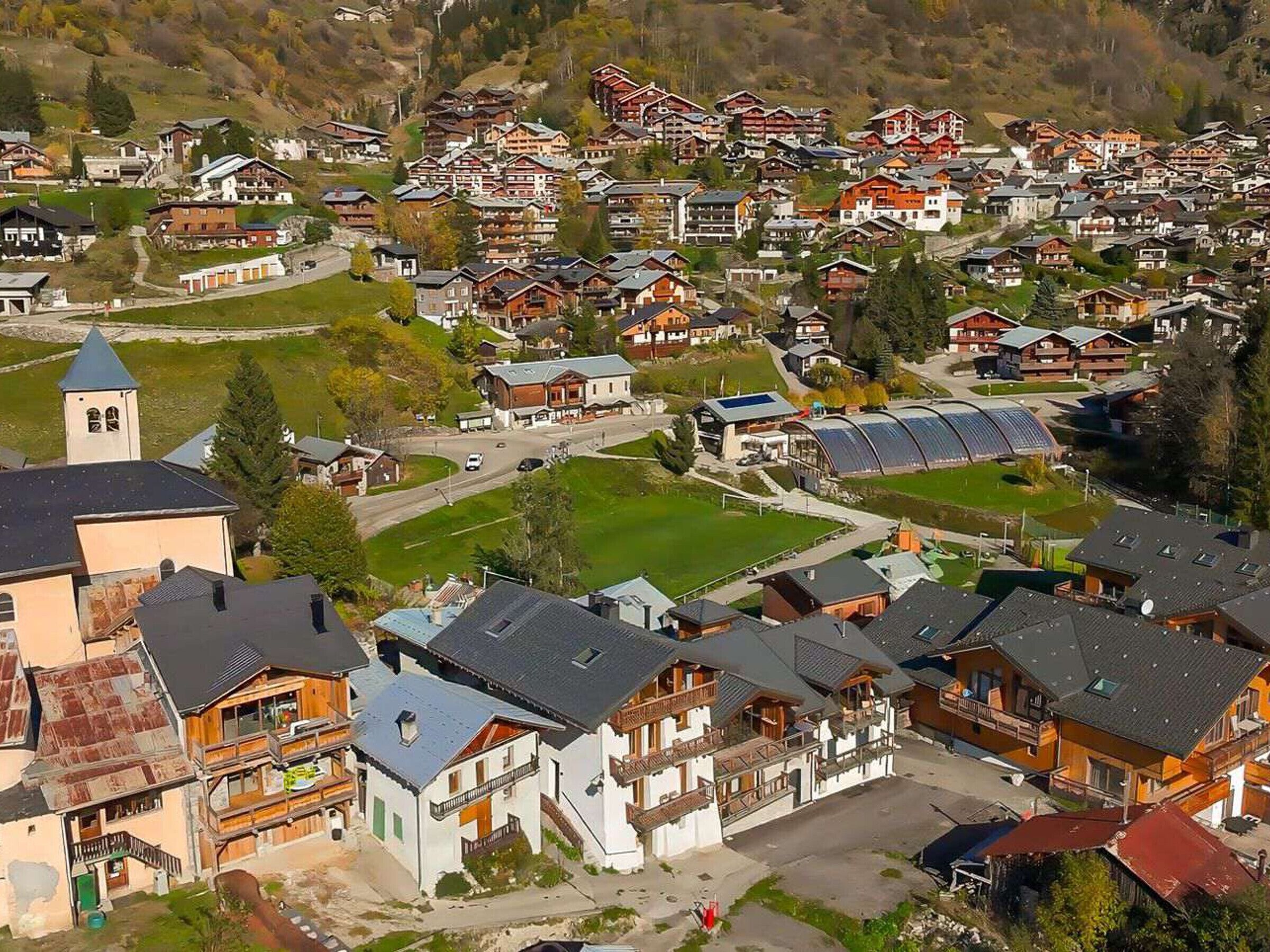 Un village avec des maisons traditionnelles en bois, une église et un terrain de sport.