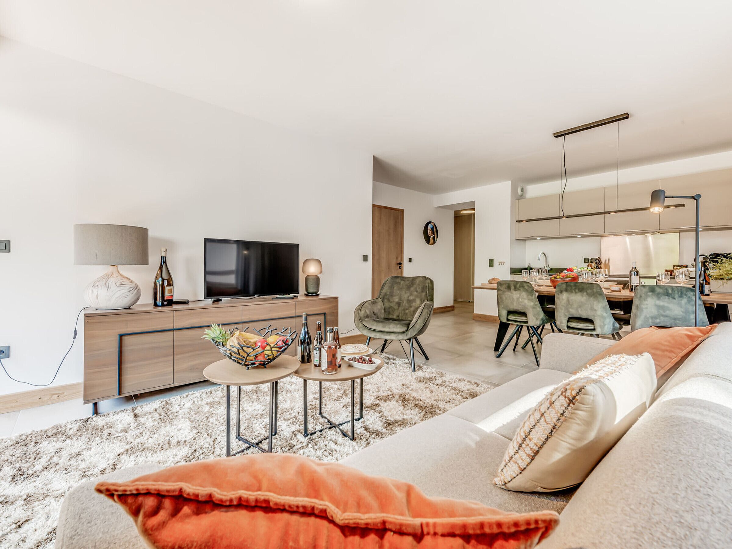 Uma sala de estar moderna com um sofá, uma mesa de centro e uma televisão. Há uma área de jantar com cadeiras e uma mesa.