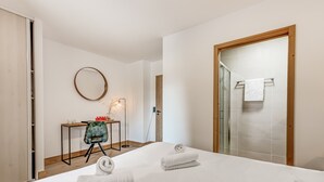 Une chambre d’hôtel comprenant un lit, un bureau avec une chaise, un miroir rond et une cabine de douche en verre.