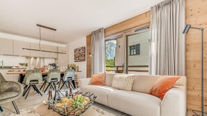 Un salon moderne avec un canapé, une table à manger et des chaises. On y trouve une grande fenêtre avec des rideaux, un lampadaire et un panier décoratif posé sur la table basse.