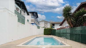 A swimming pool with a metal ladder, surrounded by a white wall and a green fence. - Renovated apartment in Hendaye with air conditioning and parking (Hendaye)
